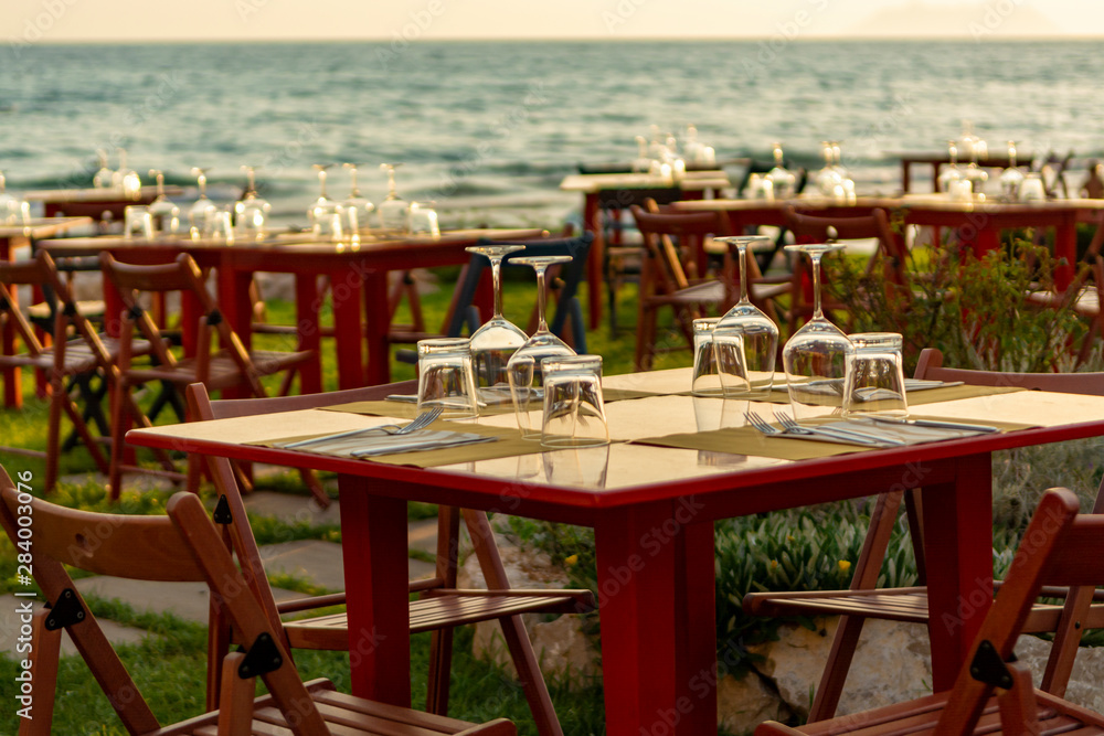 Tables in outdoor cafe or restaurant served for dinner on beach with sea view