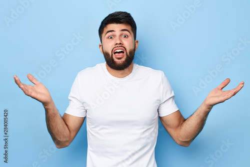 Tableau sur toile bearded young man with raised shoulders, showing ignorance on a blue background