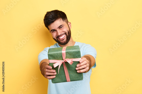 cheerful positive kind man giving a present to a friend, isolated yellow background, studio shot. kindness, positive feeling and emotion. it's for you. love, friendship concept