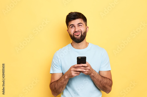 brunette handsome puzzled hesitated man using smartphone isolated over yellow background, thoughtful man doesn't want to answer the message