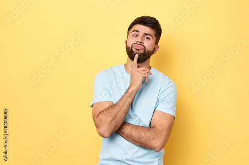 Thoughtful serious Caucasian young man touches chin with finger thinking or considering, guy making decision or imagining.close up portrait. isolated yellow background, studio shot