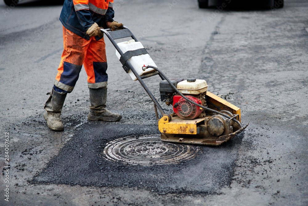 Construction worker in uniform operate vibratory plate compactor