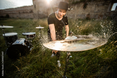 Drum plate in the grass with drops of water. Behind is a drummer emotionally plays on the drum plate