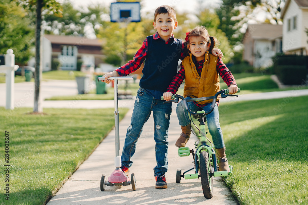Obraz premium Brother and sister in a park. Boy with scooter. Girl with bicycle.