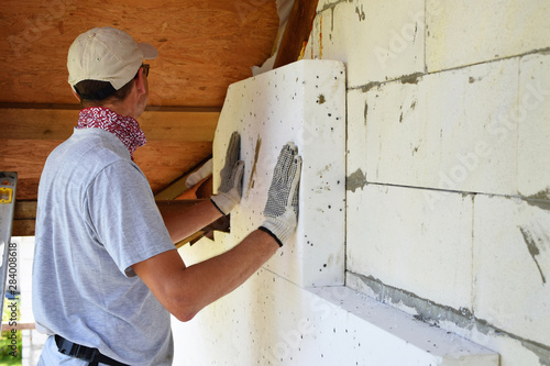 Fotografie Worker installing white rigid polyurethane foam sheet on aerated concrete block building wall facade for energy saving