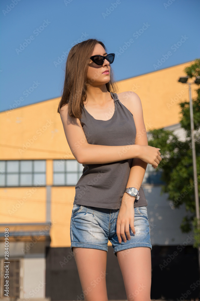 Beautiful girl with sunglasses and summer clothes looking in the sky and posing on a sunny summer day in the sunset. Urban portrait concept. Close up, selective focus Beautiful girl with sunglasses and summer clothes looking in the sky and posing on a sunny summer day in the sunset. Urban portrait concept. Close up, selective focus
