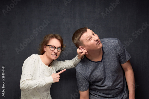 Obraz na plátně Enraged woman is pulling man by ear and scolding him