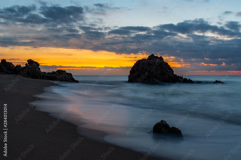 Dawn in a Mediterranean cove with reflections of the sun in the waves that caress the sand
