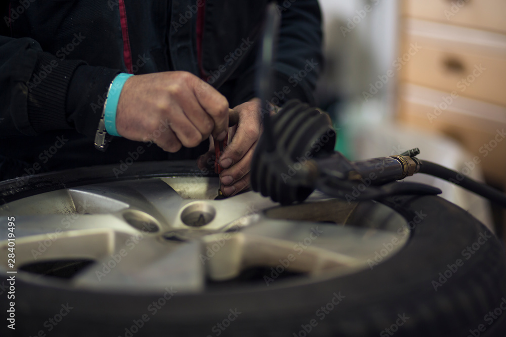 Man changing car tires in garage because of winter season. Workplace environment in dark colors, adjusting air pressure