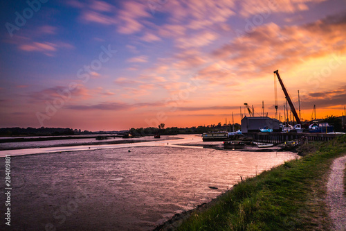 Sunset image along the bank of the river Deben with Melton boatyard in the background. The sky is a warm pastel colour
