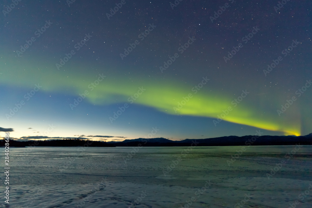 Northern Lights and morning dawn over frozen lake