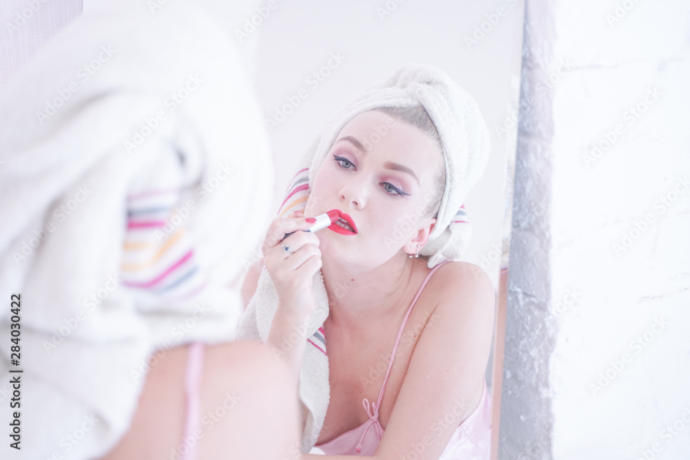 Attractive Young Woman Wrapped with Bath Towel After a Shower at the Bathroom near the mirror with lipstick Attractive Young Woman Wrapped with Bath Towel After a Shower at the Bathroom near the mirror with lipstick