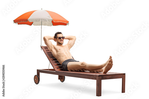 Young man lying on a sunbed under umbrella