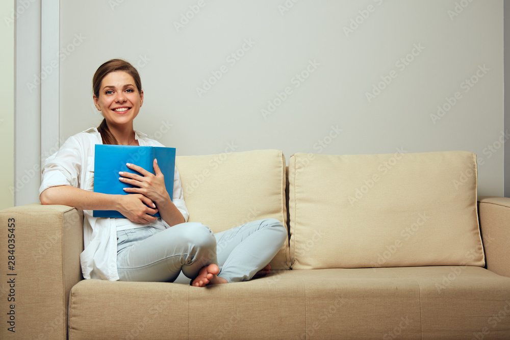 Happy woman holding open book sitting on sofa Happy woman holding open book sitting on sofa