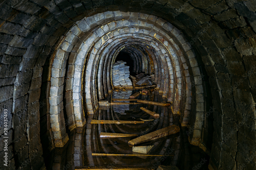 Dark creepy dirty flooded abandoned mine tunnel with remnants of rusty railway - obrazy, fototapety, plakaty 
