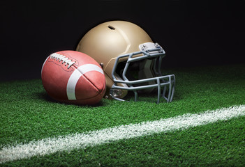 A gold football helmet and a football on a grass field with stripe on dark background