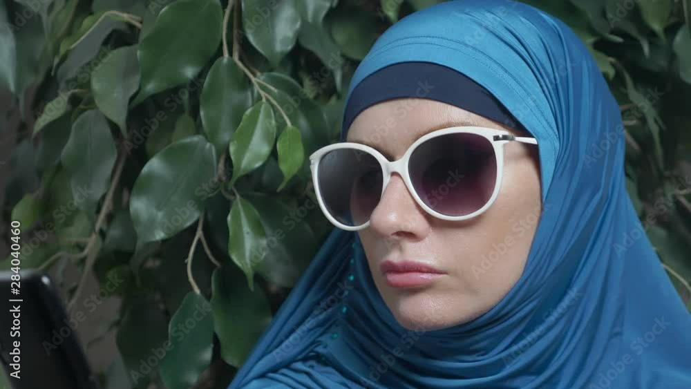 portrait of a beautiful muslim caucasian woman wearing sunglasses on a background of ficus foliage portrait of a beautiful muslim caucasian woman wearing sunglasses on a background of ficus foliage