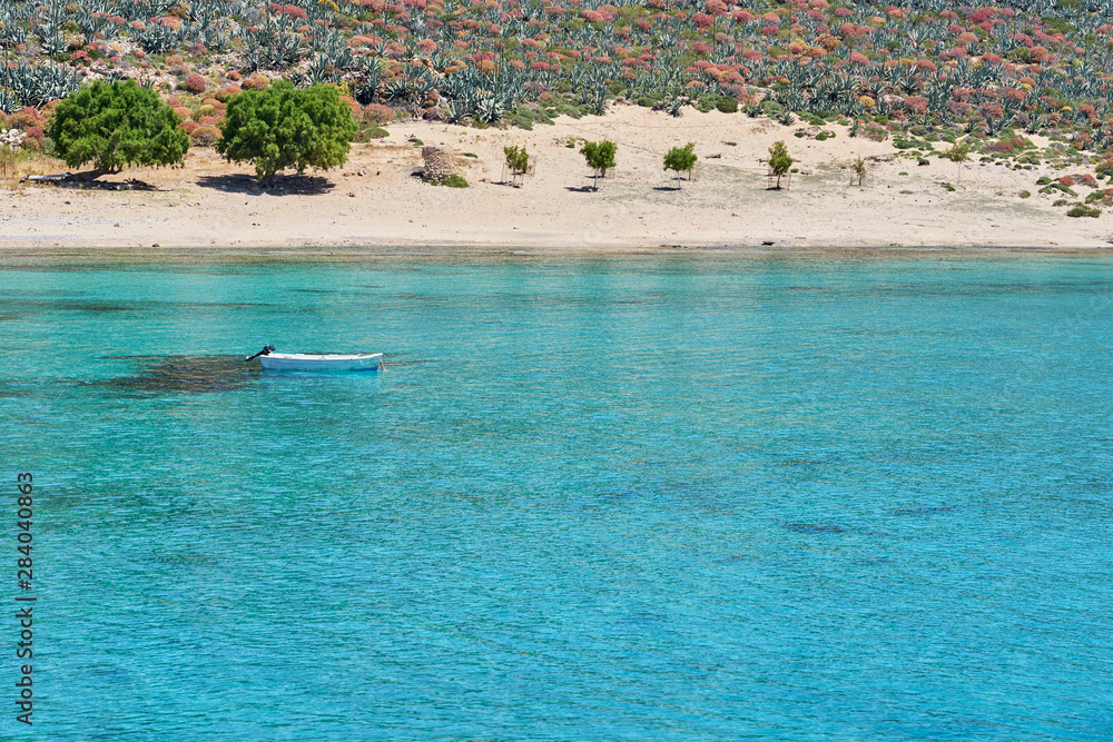A boat in turquoise water on tropical sandy beach with trees in Crete, Greece. Cope space. 