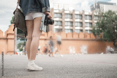 Smiling woman traveler in thapae gate landmark chiangmai thailand with backpack holding world map and camera on holiday, relaxation concept, travel concept photo