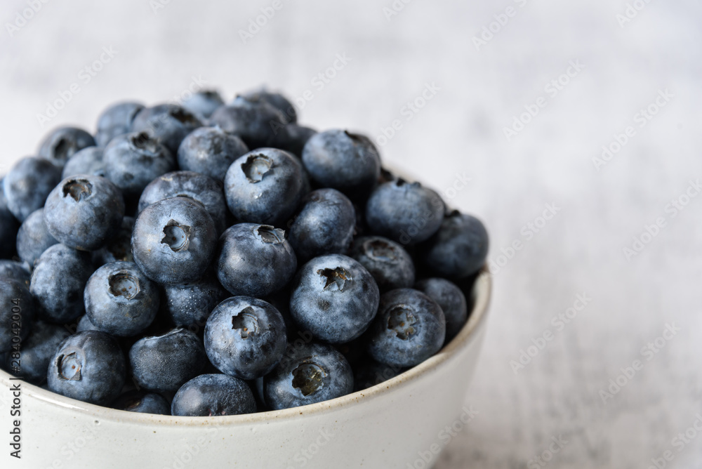 Close up of fresh blueberries in a white ceramic bowl on a light gray background Close up of fresh blueberries in a white ceramic bowl on a light gray background