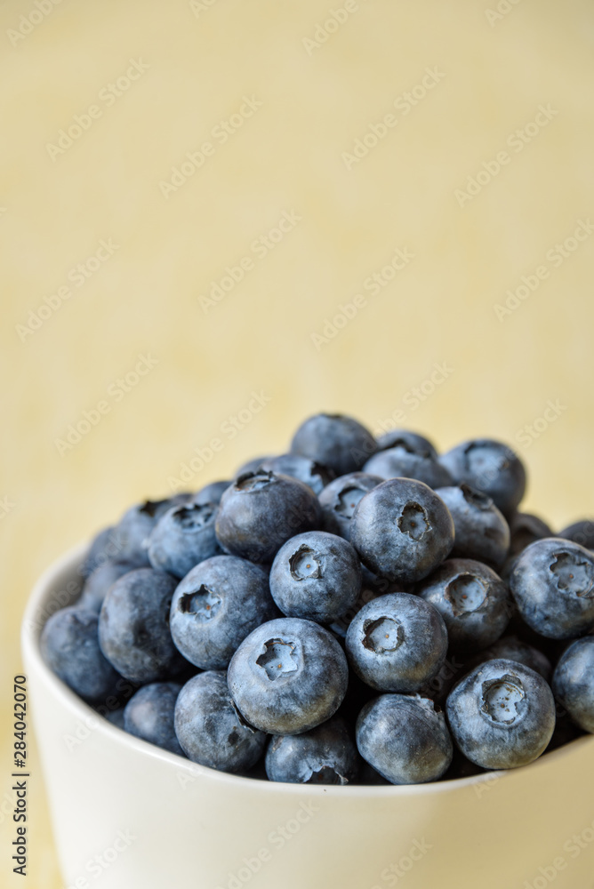 Close up of fresh blueberries in a white ceramic bowl on a yellow crackle background Close up of fresh blueberries in a white ceramic bowl on a yellow crackle background