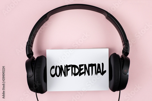 Handwriting text Confidential. Concept meaning Agreements between two parties are private and protected written White Sticky Note paper plain Pink background Headphone next to it. photo