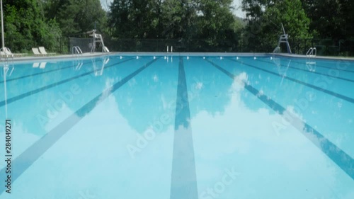 Tilt to reveal a deserted outdoor olympic size swimming pool. The empty training pool waits for swimmers to arrive and start training. Low angle represents budget cuts, funding shortages and athletes 