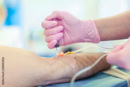 Preparation for surgery. Medical nurse with pink latex gloves inputs catheter to vein patient for drip of chemotherapy or another liquid medicine, jection of propofol to patient for iv anesthesia.