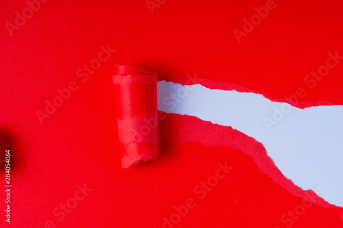 Torn red coloured paper on white background with closeup hole in the sheet of paper. Background concept with copy space.