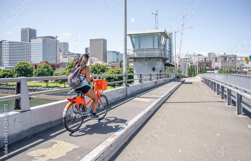 Young girl with long hair rides a bicycle on a bridge and simultaneously texting on the phone