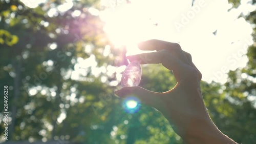 Female hand with transparent amethyst quartz yoni egg for vumfit, imbuilding or meditation. Shining crystal egg in hands on sky and sunrise background outdoors. Womens health concept.
