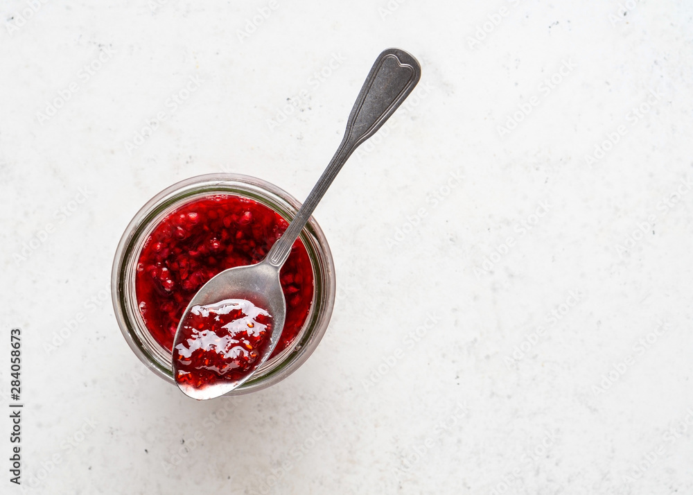 Glass jar of homemade raspberry jam on white stone background. Glass jar of homemade raspberry jam on white stone background.