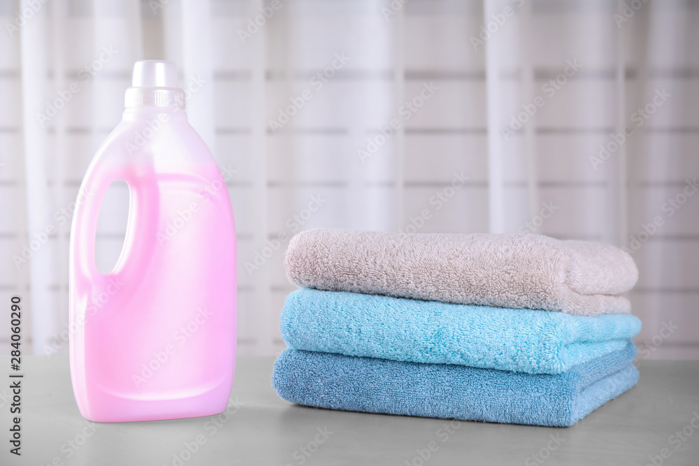 Clean towels and bottle of laundry detergent on table against blurred background Clean towels and bottle of laundry detergent on table against blurred background
