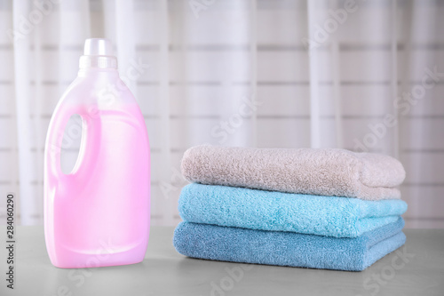 Clean towels and bottle of laundry detergent on table against blurred background