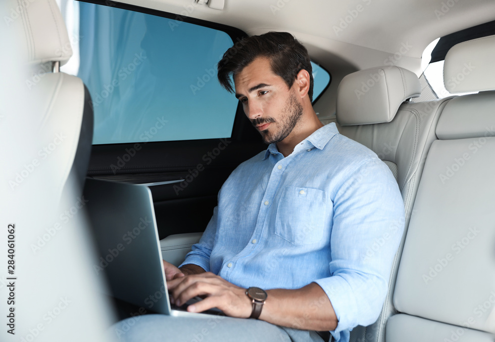 Attractive young man working with laptop on backseat in luxury car Attractive young man working with laptop on backseat in luxury car