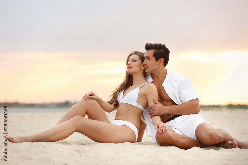 Happy young couple relaxing together on sea beach at sunset