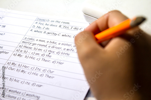Close-up of boy hand with pencil writing English words by hand on traditional white notepad paper. The boy writes his first test on English. Child writing