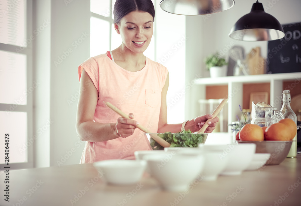 Smiling young woman mixing fresh salad in the kitchen.