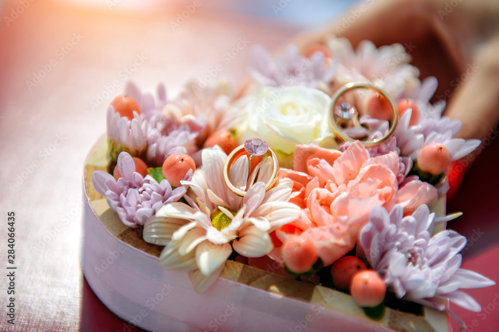Wedding rings lie among fresh flowers in small wooden box, close up. Gold wedding rings on flower background, selective focus. Wedding rings lie among fresh flowers in small wooden box, close up. Gold wedding rings on flower background, selective focus.