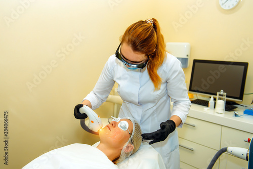 Doctor conducts procedure for rejuvenating facial skin with laser. Woman receiving facial beauty treatment, removing pigmentation at clinic. Intense pulsed light therapy. IPL. Anti-aging Procedures.