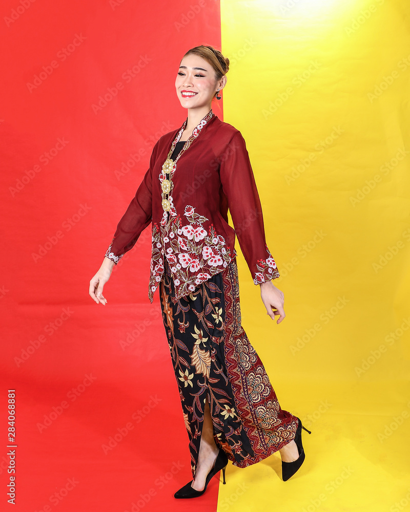 Asian woman traditional maroon kebaya sharong on red yellow paper background walk forward