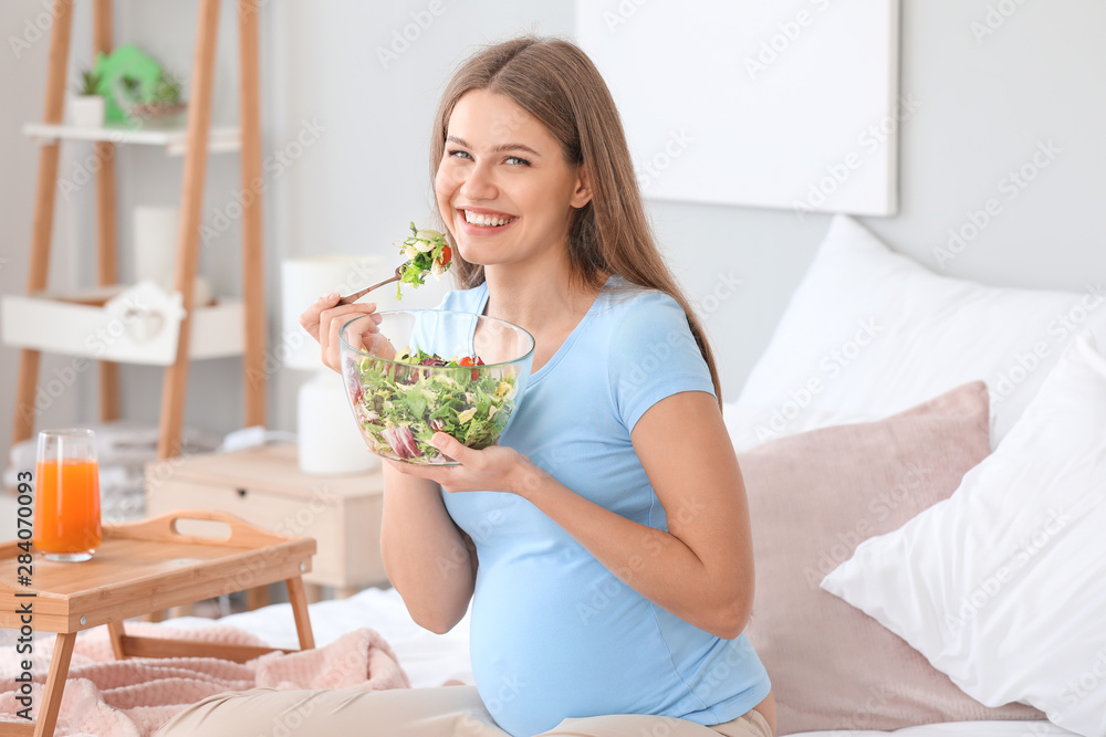 Beautiful pregnant woman having breakfast in bedroom