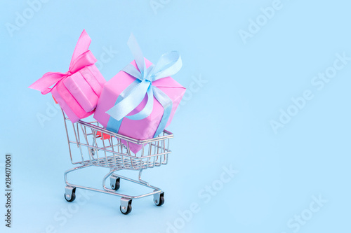 Gift in pink box with satin ribbon in shopping cart on blue background, congratulations on Women's Day, mum's day, Valentine's day, happy birthday, Christmas