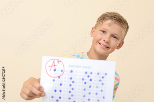 Happy boy with answer sheet for school test on light background photo