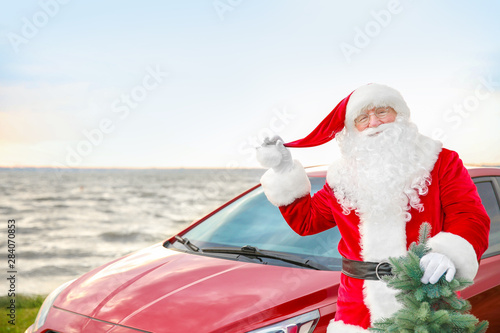 Santa Claus with fir tree near car on riverside © Pixel-Shot
