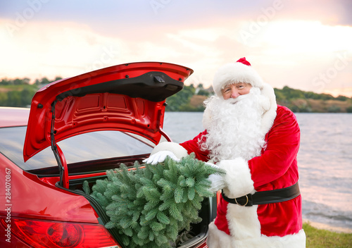 Santa Claus putting fir tree into car trunk on riverside © Pixel-Shot