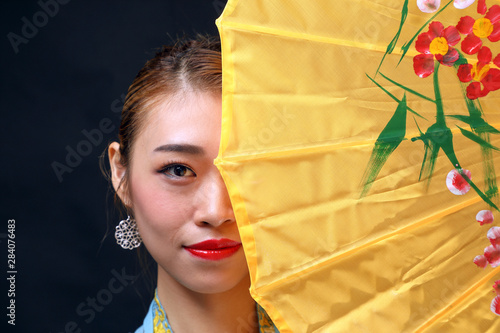 Asian woman in tractional kebaya behind umbrella on black background © oqba