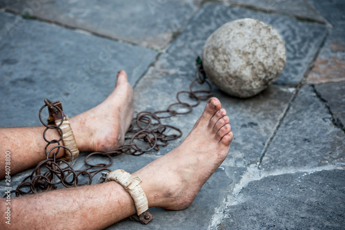 Prisioner with ball and chain in the court of the prison. Close up. Concept of inhuman and degrading detention conditions.