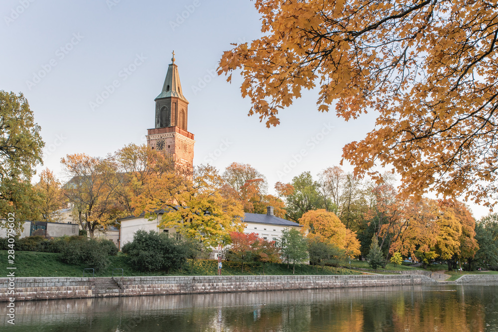 Beautiful fall foliage and Aura river against clear blue sky with Turku Cathedral in background in Turku, Finland, Autumn 2018