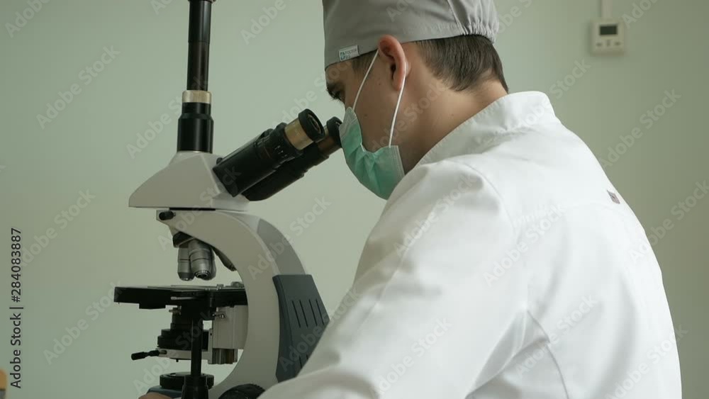 Close-up of a doctor looking through a microscope in a bandage in the uniform of a doctor. Medical analysis. Microscopic examination. Close-up of a doctor looking through a microscope in a bandage in the uniform of a doctor. Medical analysis. Microscopic examination.